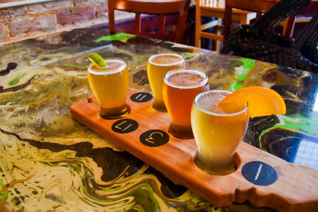 Four glasses of beer in a wooden platter on top of a table