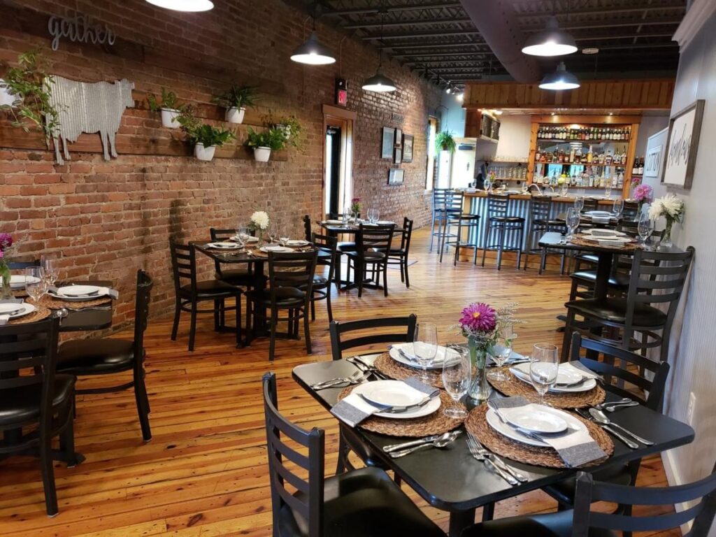 The interior of a restaurant with black tables and chairs all set with dishes, cutlery and glassware