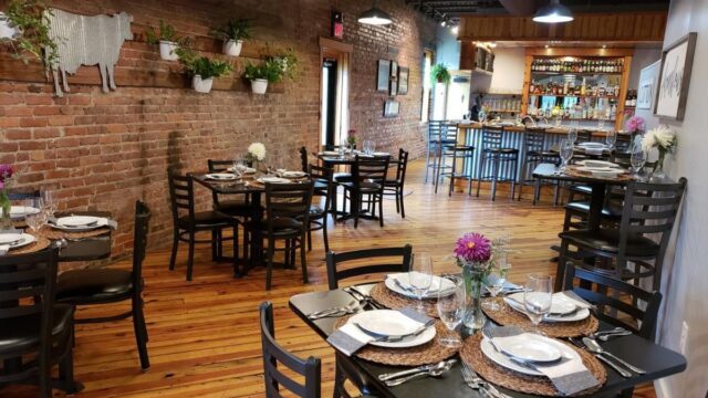 The interior of a restaurant with black tables and chairs all set with dishes, cutlery and glassware