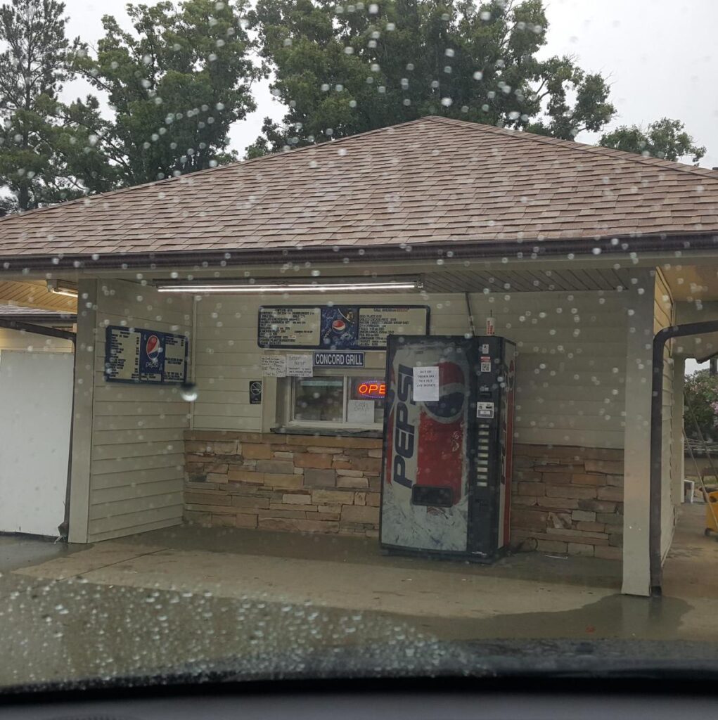 A service window for Concord Grill next to a soda vending machine