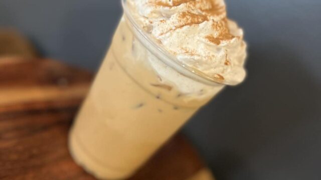 An iced coffee topped with whipped cream in a plastic cup sits on a wooden table