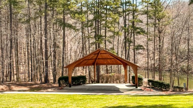 A wooden gazebo surrounded by green grass and tall trees