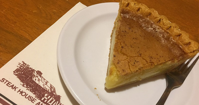 A slice of buttermilk pie and a fork on a white plate