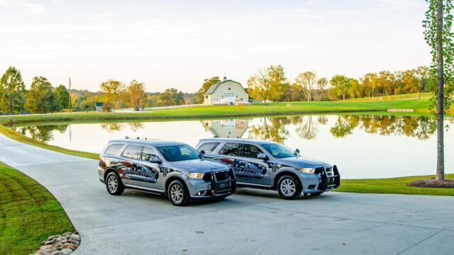 Two silver police cars parked on a concrete driveway by a lake