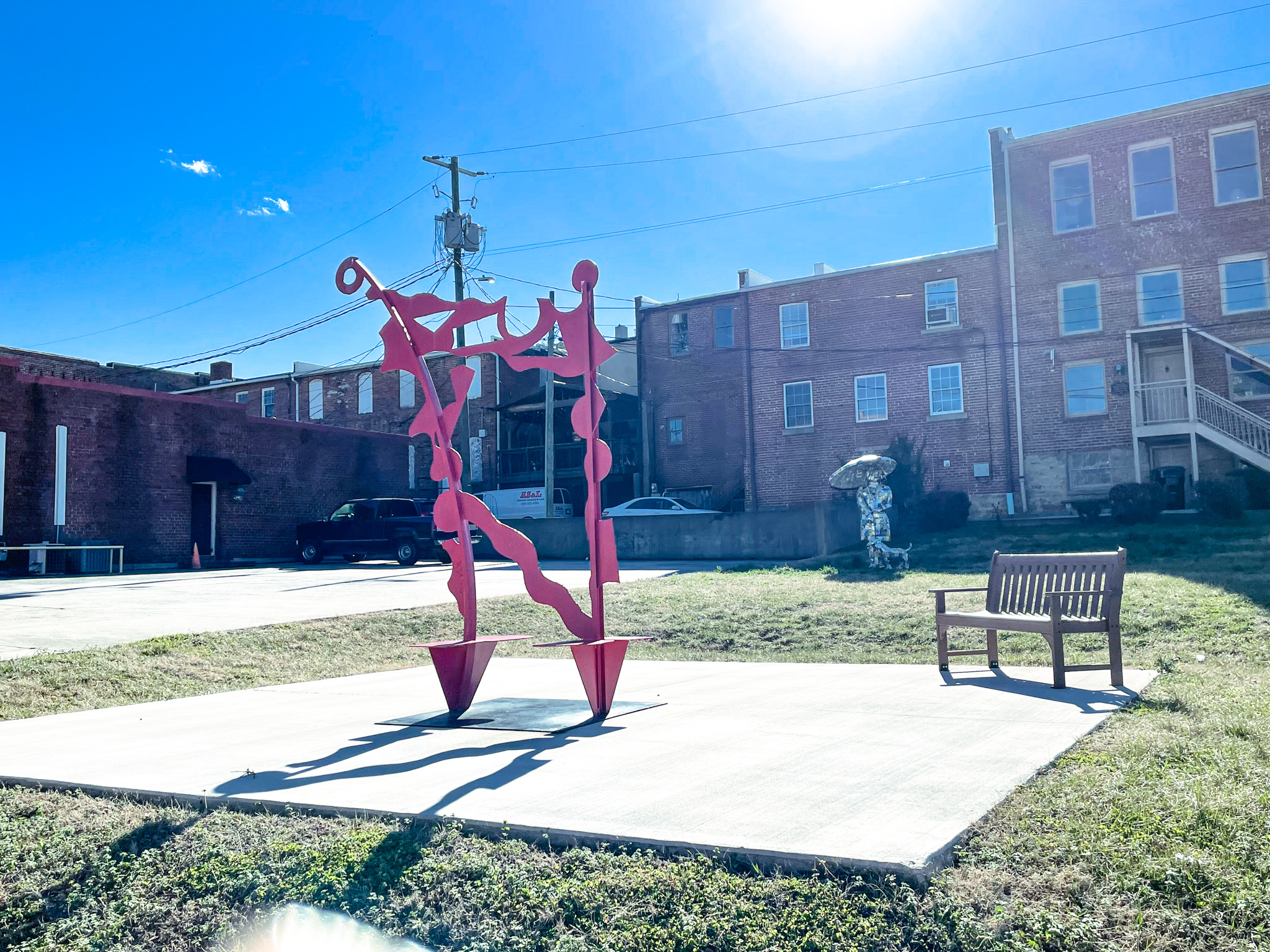A red metal art sculpture on a concrete pad with a bench nearby