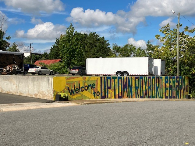 A mural reading 'Welcome to Uptown Roxboro Person County' painted in a cement wall